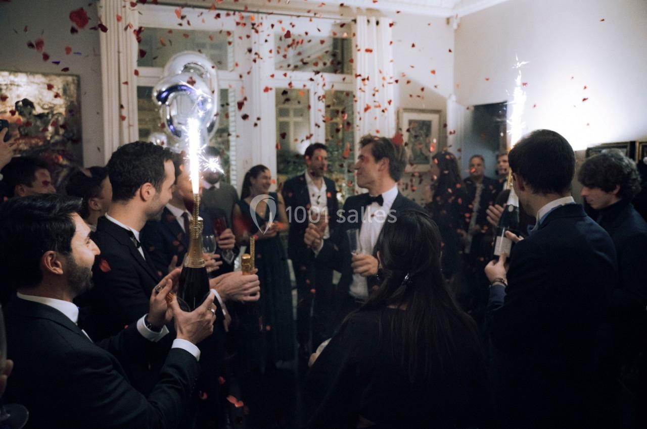 Groupe de personnes en tenue de soirée célébrant avec des bouteilles de champagne et des confettis dans une pièce décorée.