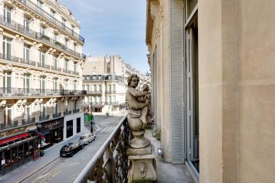 Table ronde en métal noir avec chandelier et chaises, placée sur un balcon avec vue sur une façade d'immeuble haussmannien.
