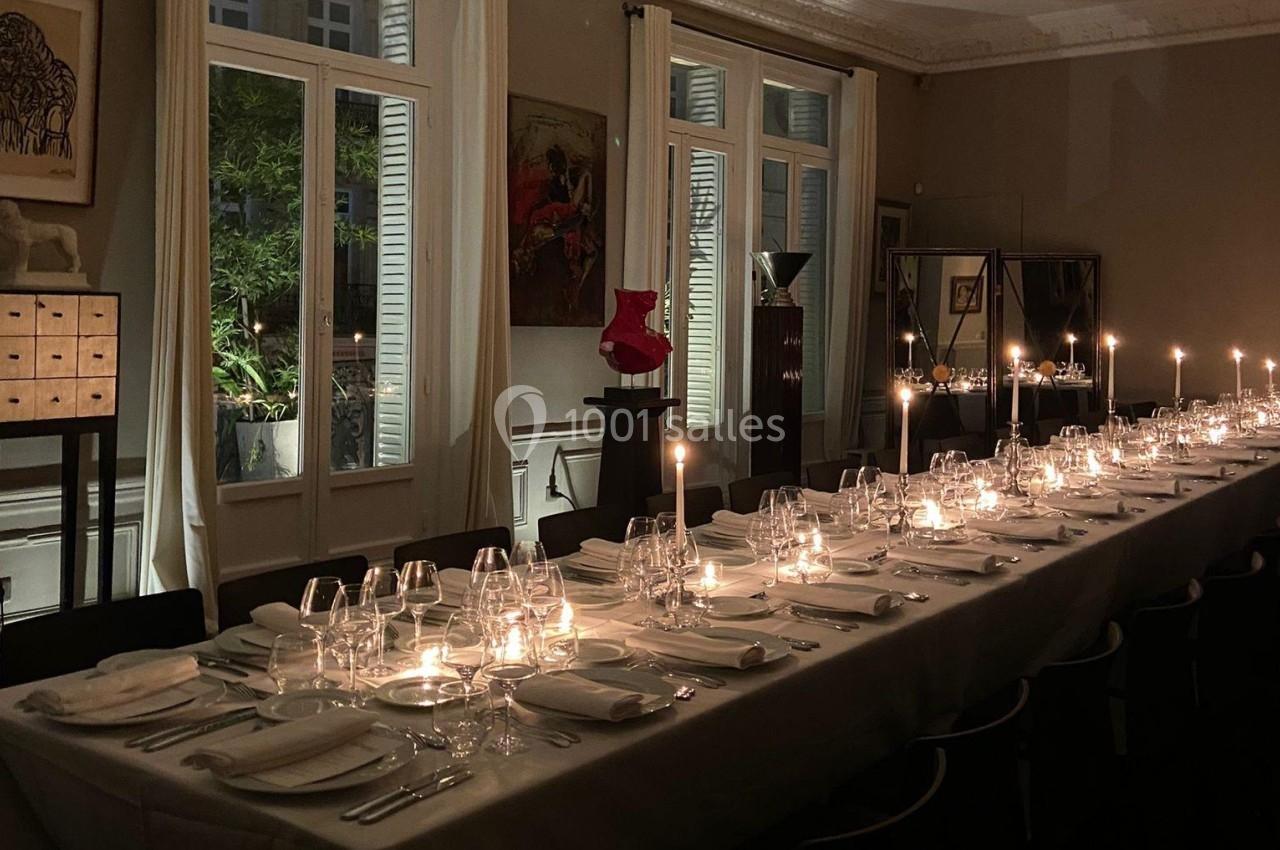Table élégamment dressée avec des bougies allumées dans une salle à manger aux grandes fenêtres donnant sur un jardin.