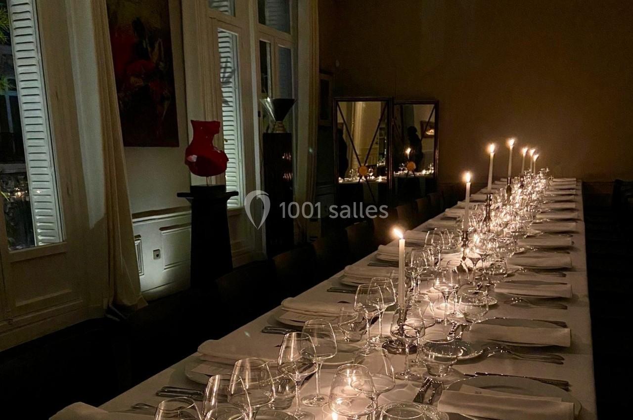 Table élégamment dressée avec des bougies allumées, verres et couverts dans une salle à l'éclairage tamisé.