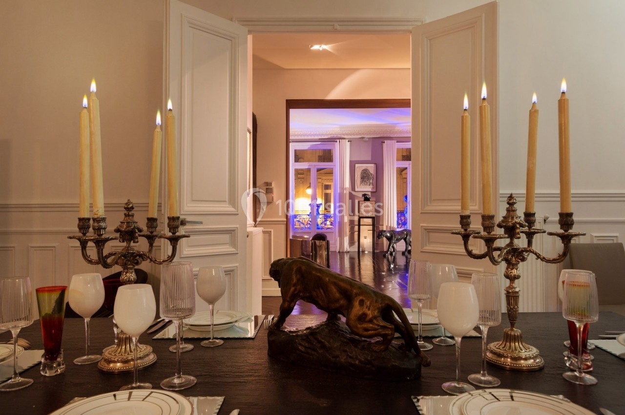 Table dressée avec chandeliers, verres et statue de panthère, dans une salle à manger élégante avec portes ouvertes.
