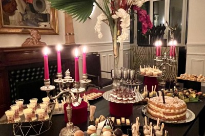 Table ronde en métal noir avec chandelier et chaises, placée sur un balcon avec vue sur une façade d'immeuble haussmannien.