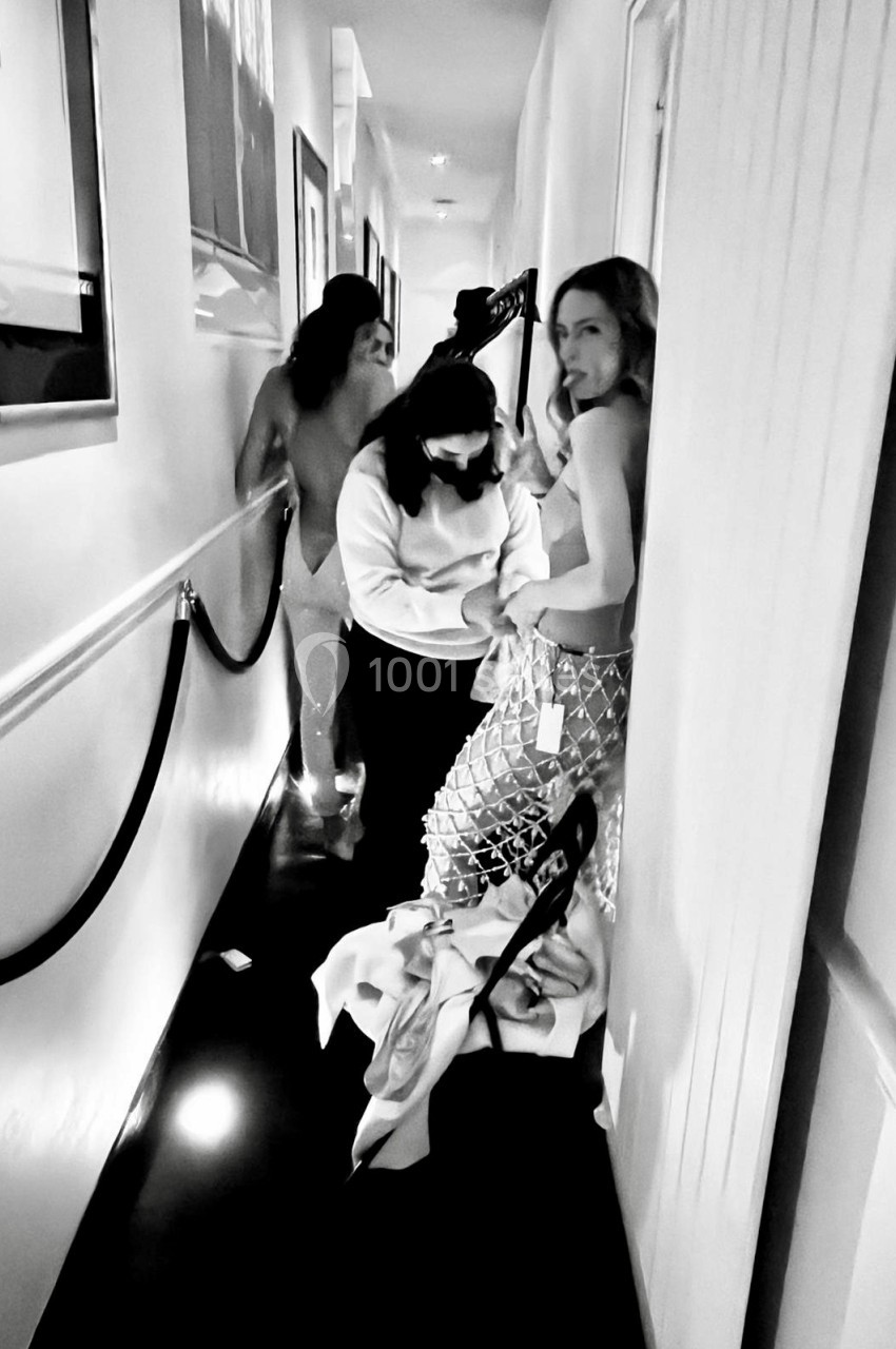 Une femme ajuste une tenue sur une autre femme dans un couloir étroit, entourées de vêtements et d'accessoires.