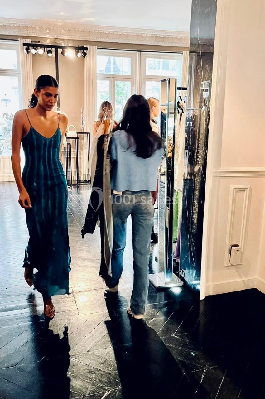Deux femmes dans une boutique lumineuse, l'une portant une robe bleue, l'autre tenant des vêtements sur cintres.