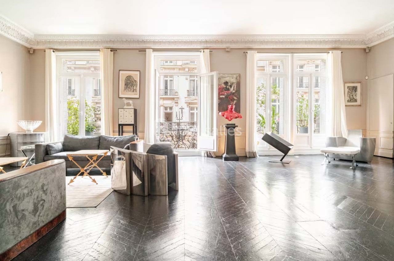 Salon lumineux avec parquet en chevrons, mobilier moderne, grandes fenêtres et vue sur des immeubles haussmanniens.