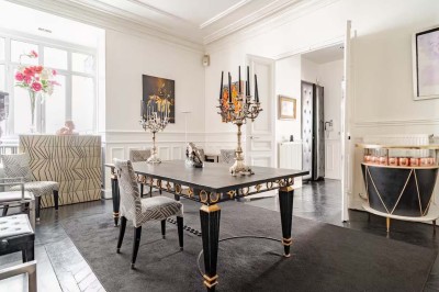 Table ronde en métal noir avec chandelier et chaises, placée sur un balcon avec vue sur une façade d'immeuble haussmannien.