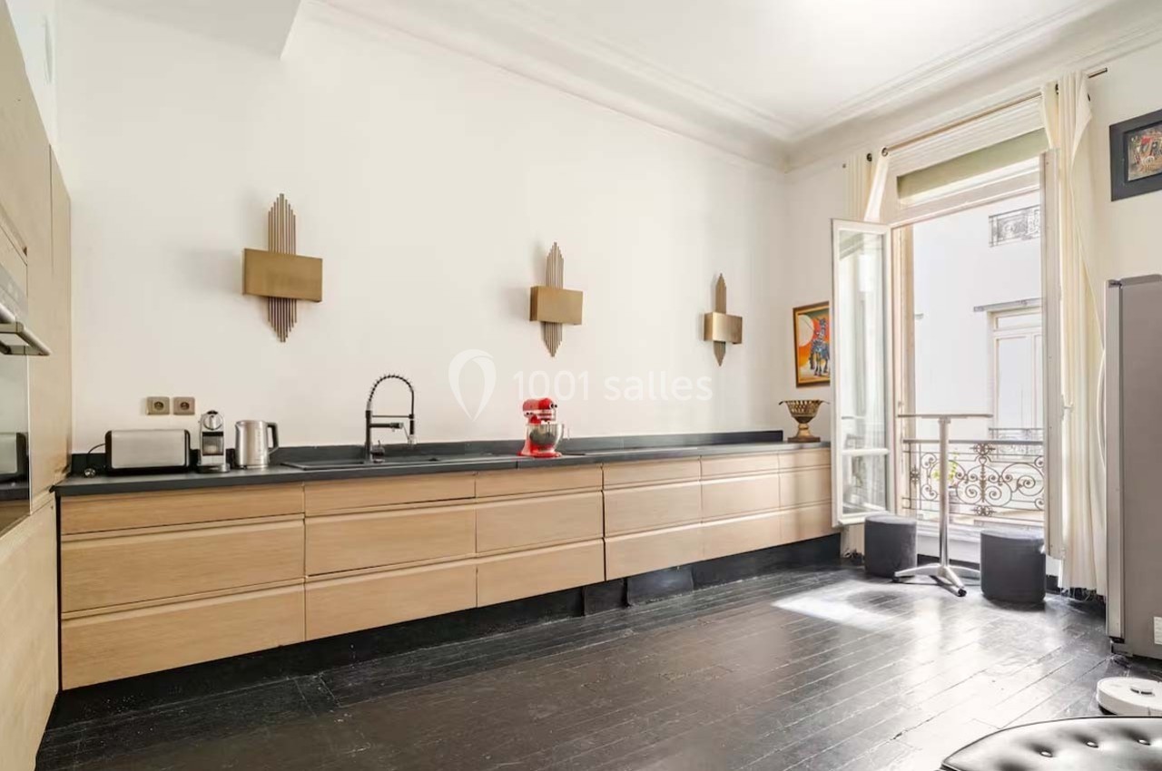 Cuisine lumineuse avec meubles en bois clair, plan de travail noir, électroménagers modernes et fenêtre ouverte sur un…