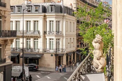 Table ronde en métal noir avec chandelier et chaises, placée sur un balcon avec vue sur une façade d'immeuble haussmannien.
