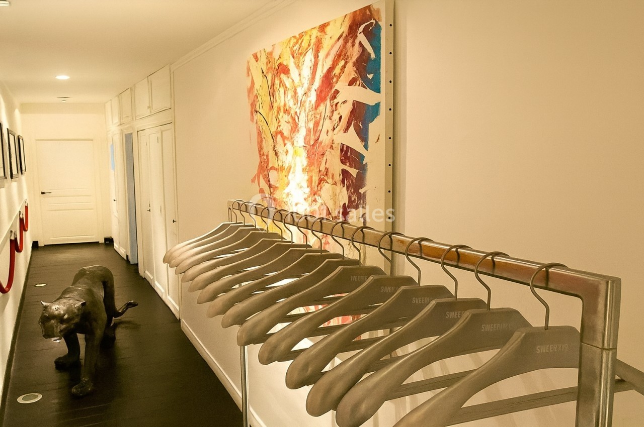 Portant avec des cintres vides dans un couloir lumineux, décoré d'une peinture abstraite et d'une sculpture de panthère.