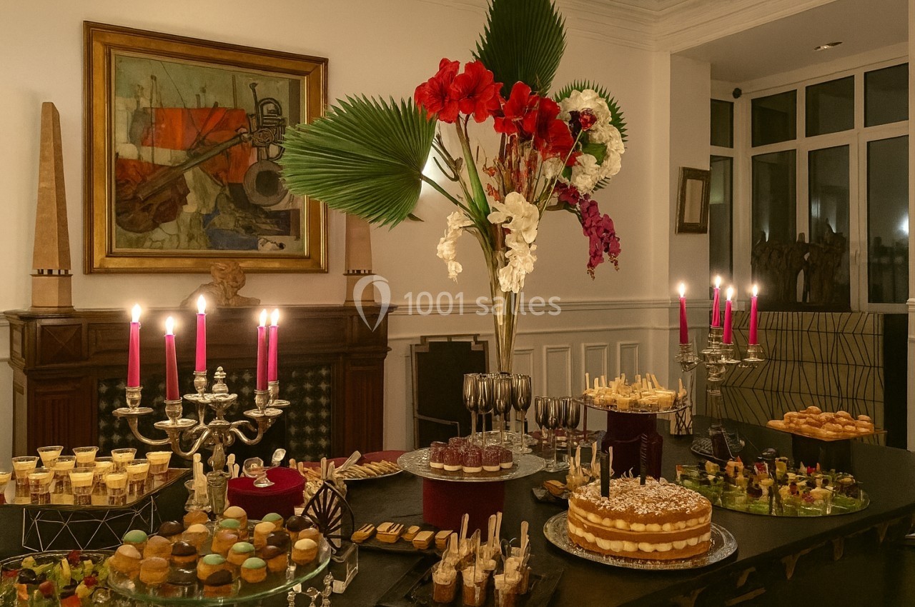 Table garnie de desserts variés, bougies allumées et grand bouquet de fleurs rouges et blanches en décoration.
