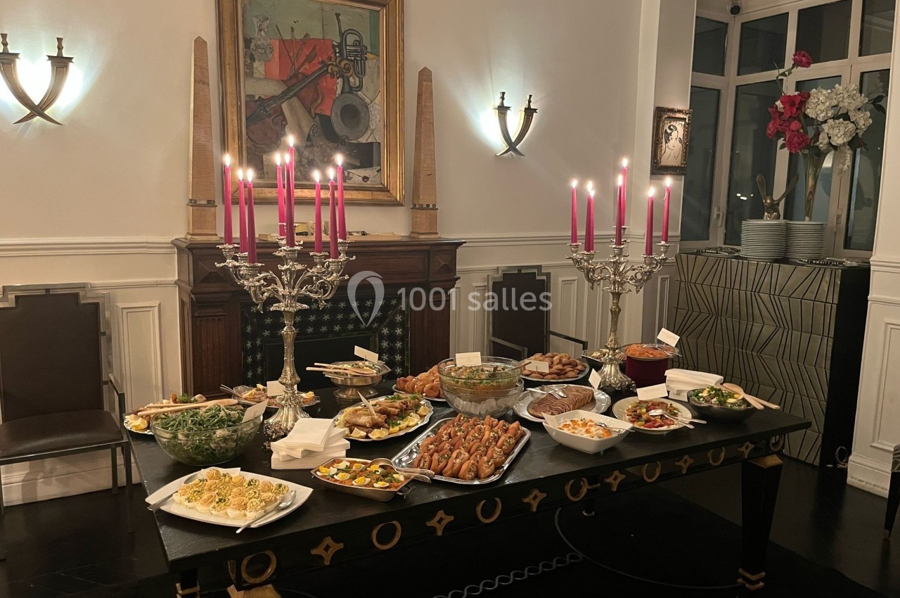 Location salle Paris 8 (Paris) - Le Loft Triangle d'Or Champs-Élysées #40 Table dressée avec divers plats et bougeoirs ornés de bougies roses, dans une salle élégante avec cheminée et décorations…