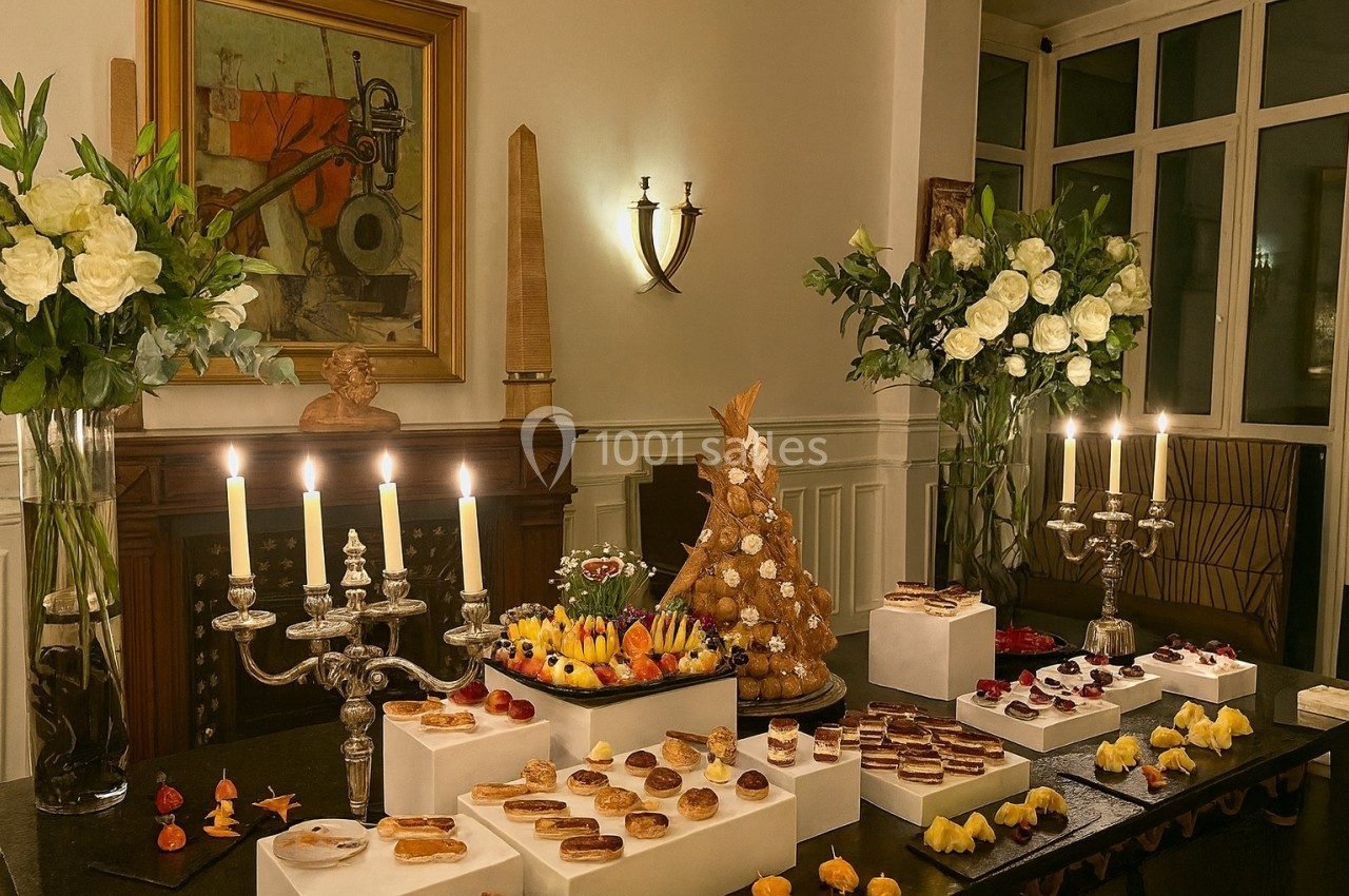 Location salle Paris 8 (Paris) - Le Loft Triangle d'Or Champs-Élysées #44 Table garnie de pâtisseries variées, éclairée par des chandeliers, avec des fleurs et une pièce montée en arrière-plan.