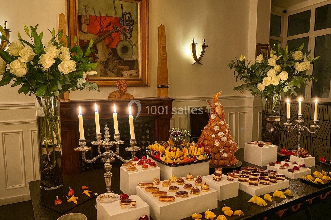 Location salle Paris 8 (Paris) - Le Loft Triangle d'Or Champs-Élysées #49 Table décorée avec des chandeliers, fleurs blanches et desserts variés, dont une pièce montée, dans une salle élégante.