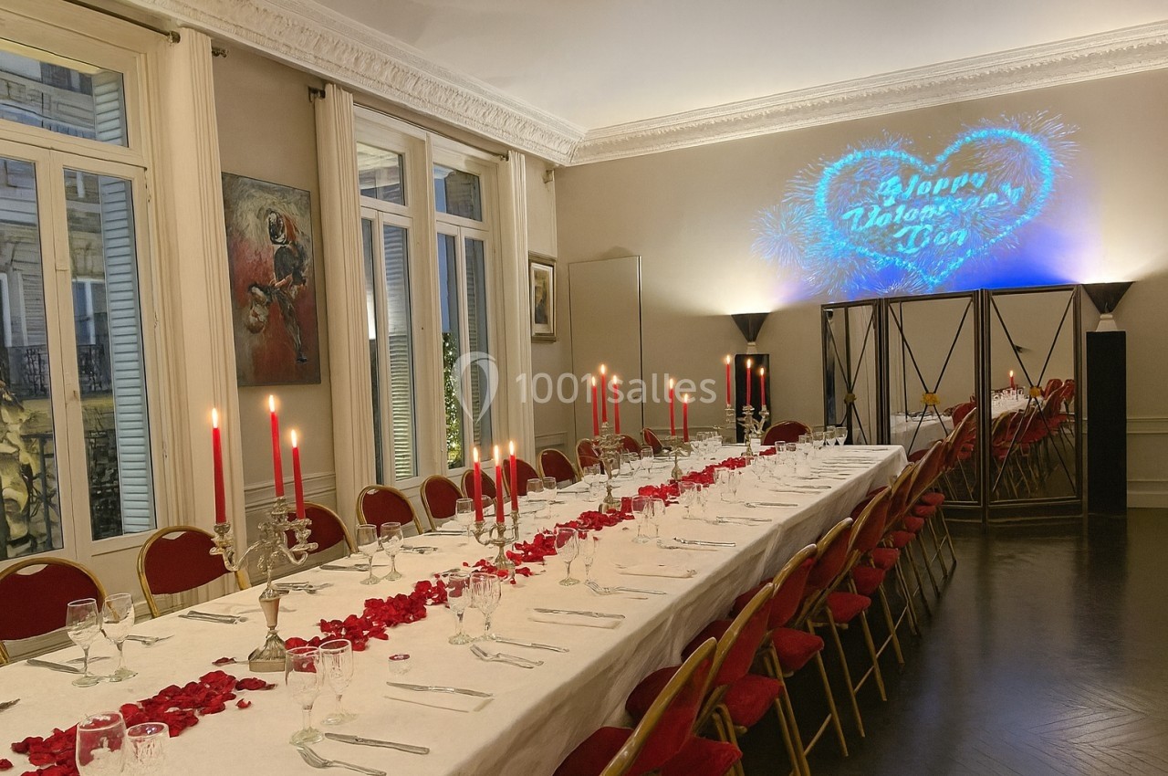 Location salle Paris 8 (Paris) - Le Loft Triangle d'Or Champs-Élysées #50 Grande table de banquet décorée de pétales de roses et bougies rouges, dans une salle élégante avec projection murale.