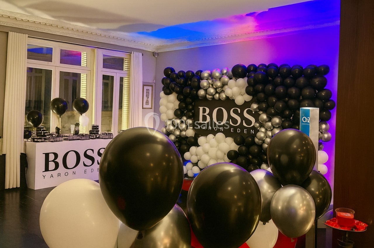 Location salle Paris 8 (Paris) - Le Loft Triangle d'Or Champs-Élysées #51 Mur de ballons noirs, blancs et argentés décorant une salle avec une table et un logo ’Boss Yaron Eden’.