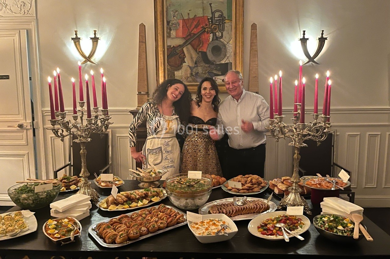 Location salle Paris 8 (Paris) - Le Loft Triangle d'Or Champs-Élysées #55 Trois personnes souriantes posent devant une table garnie de plats variés dans une salle élégamment décorée.