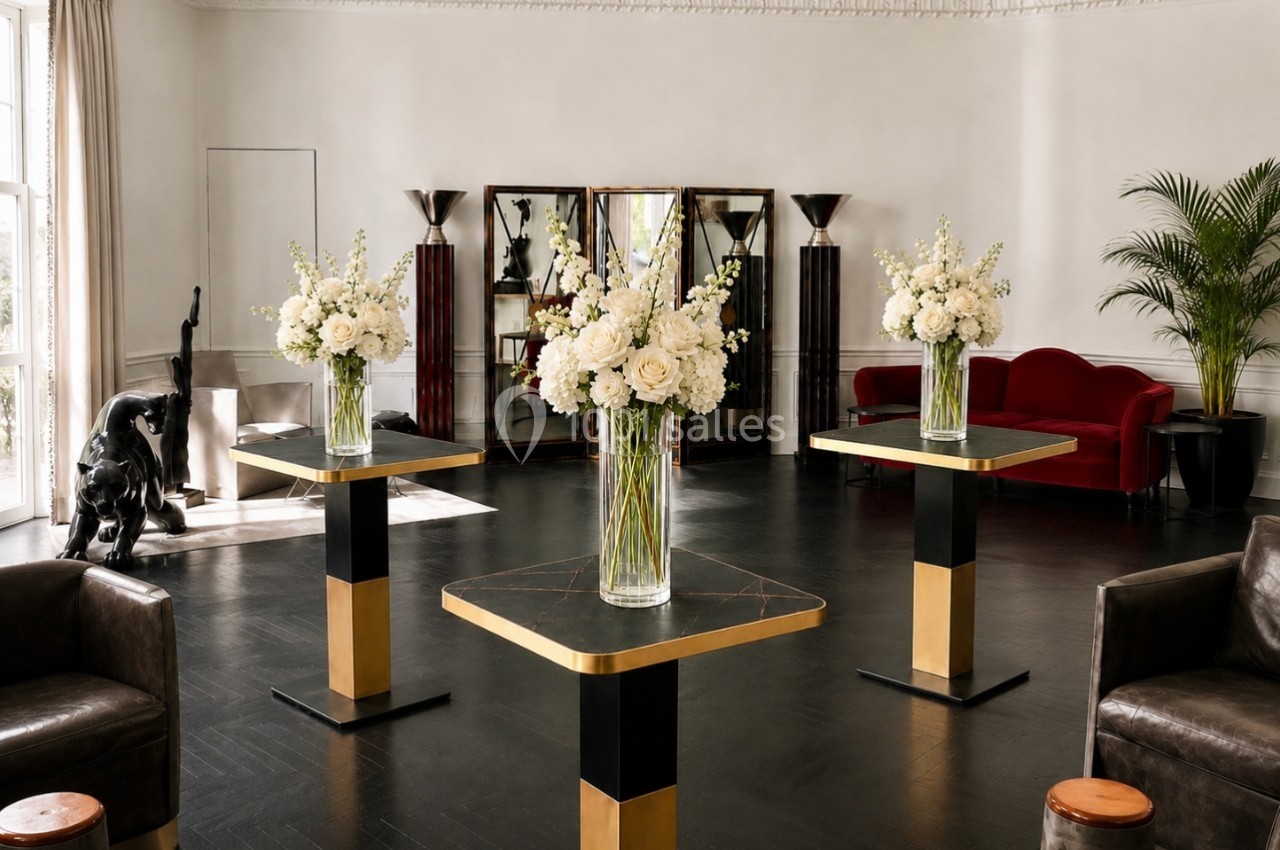 Salle élégante avec tables modernes ornées de bouquets blancs, canapé rouge, statue et plantes en arrière-plan.
