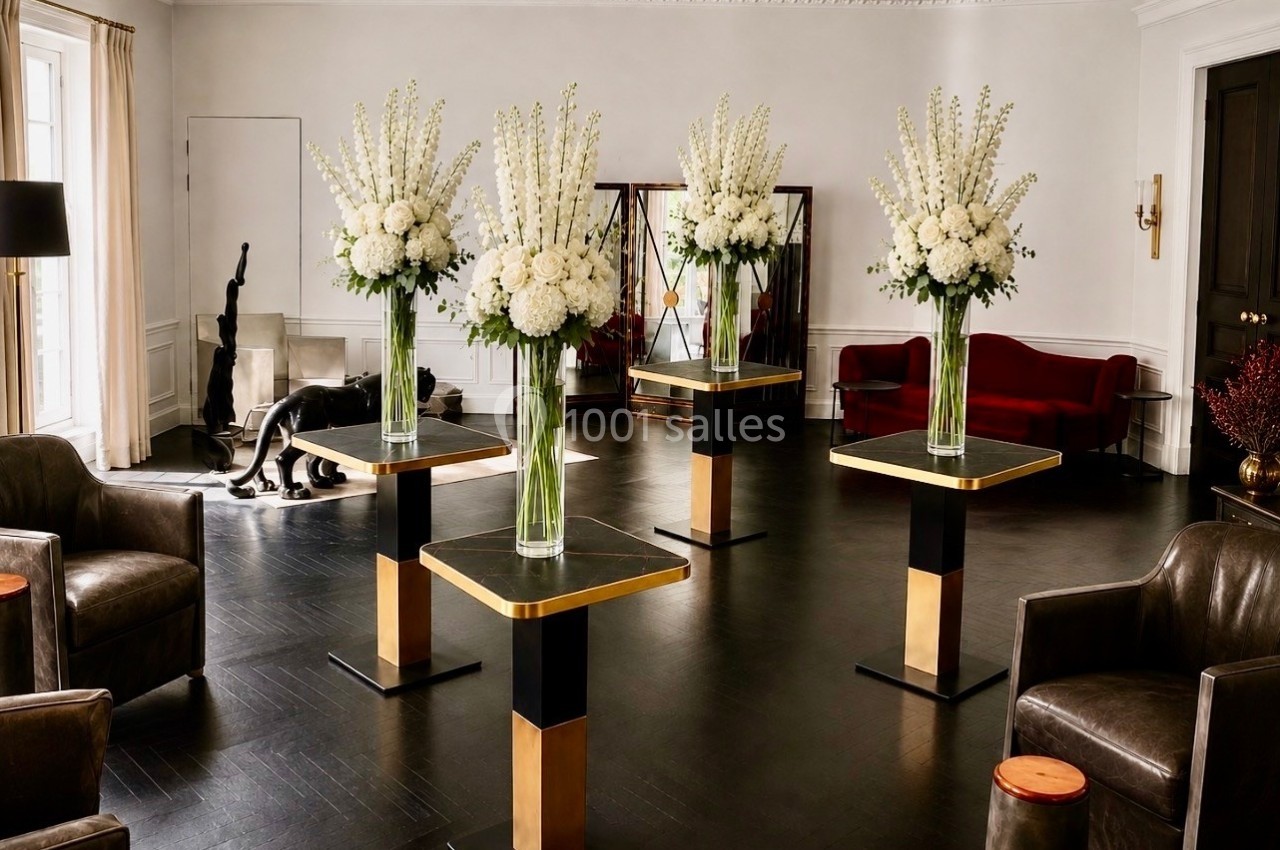 Salle élégante avec quatre compositions florales blanches sur des tables modernes, entourées de fauteuils et d'un canapé…