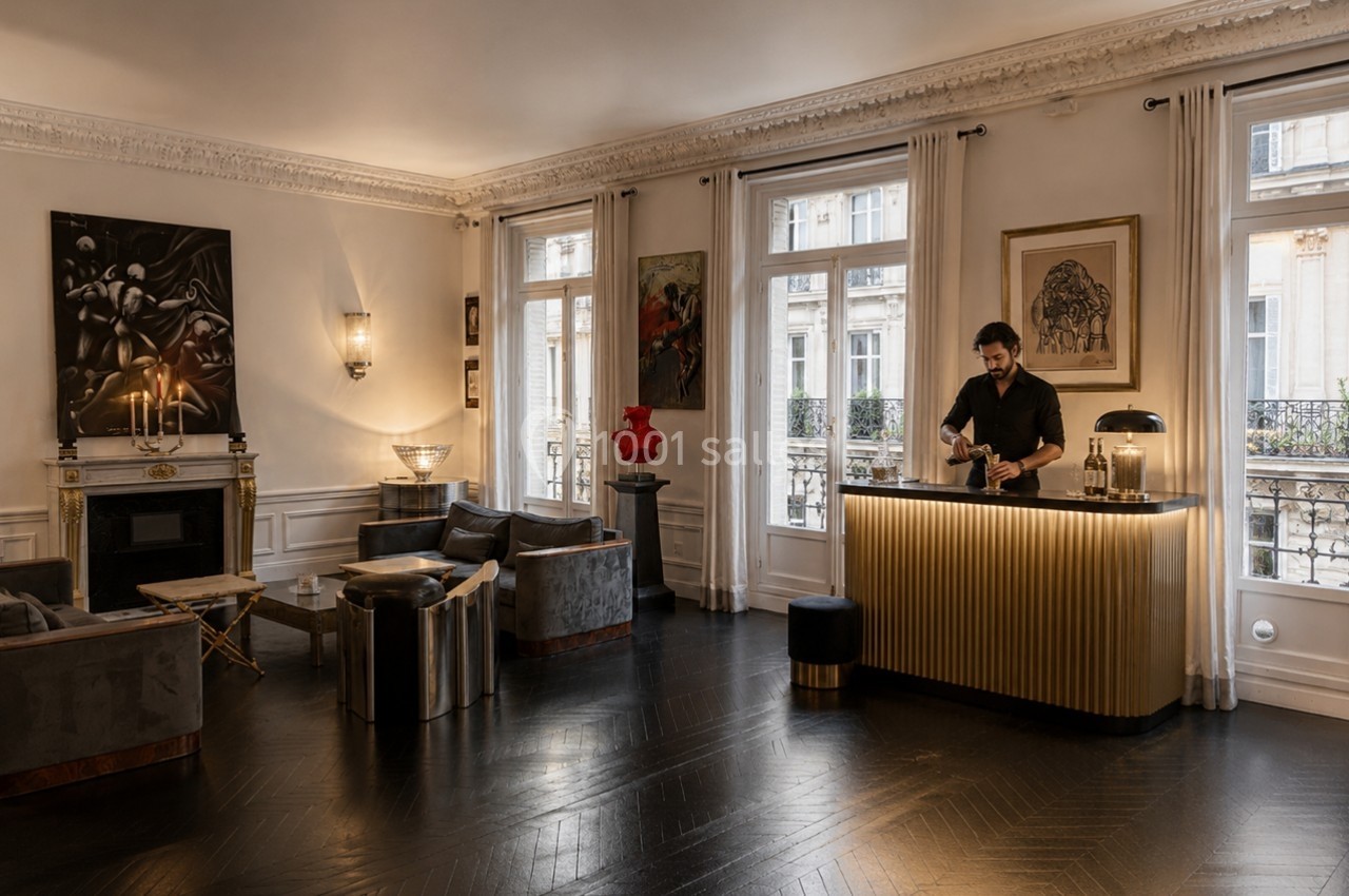 Un homme prépare une boisson derrière un comptoir doré dans un salon élégant avec parquet sombre et œuvres d'art.