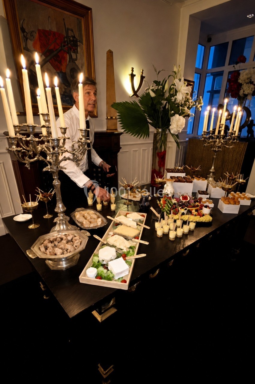 Table de buffet élégante avec chandeliers, plats variés et serveur en arrière-plan dans une salle éclairée.