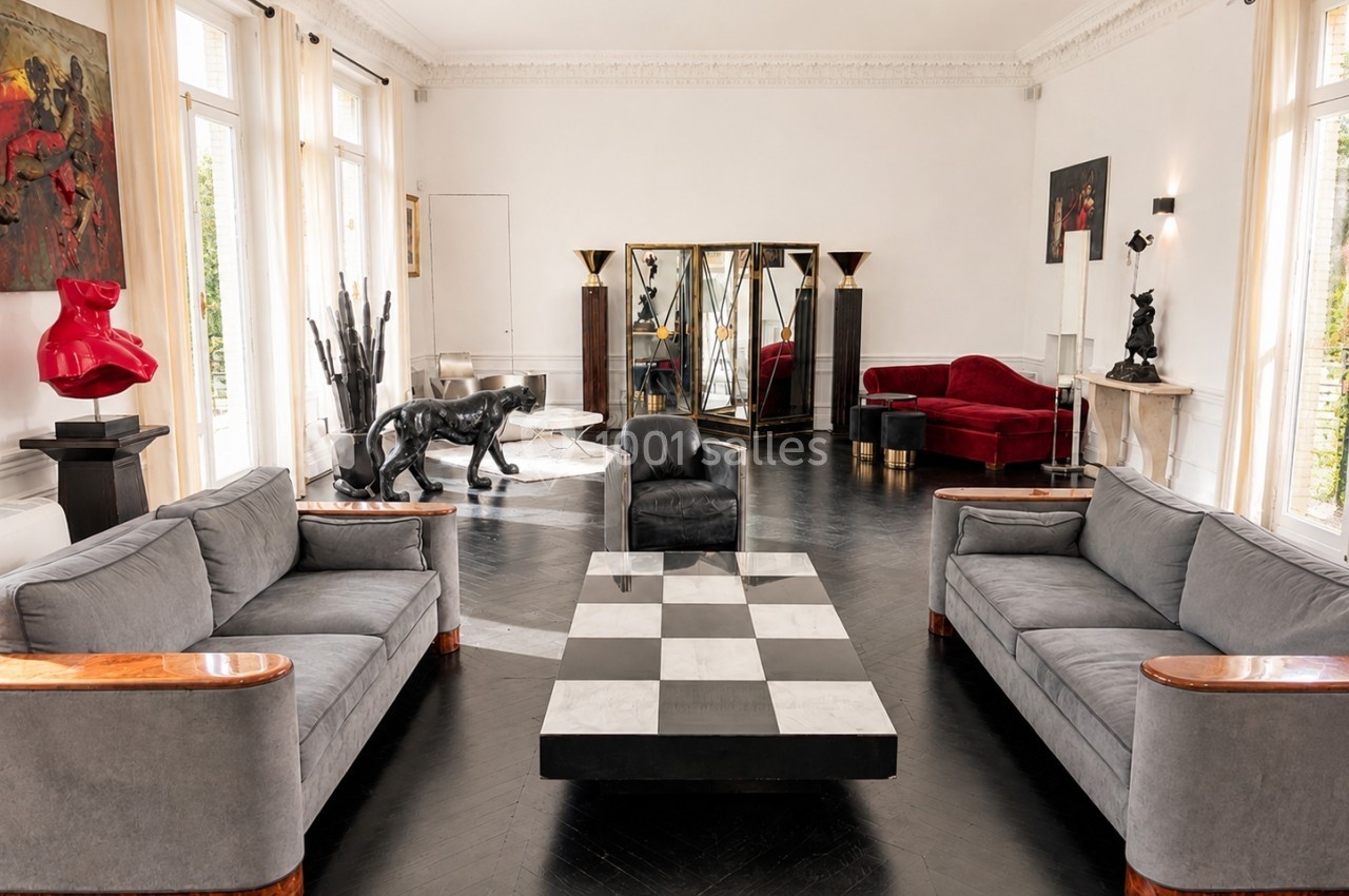 Salon spacieux avec mobilier design, canapé gris, table basse damier, sculptures et miroirs décoratifs.