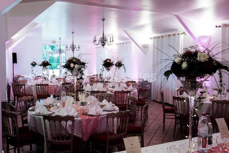 Salle de réception décorée avec des tables rondes, nappes blanches, chaises en bois et centres de table fleuris.