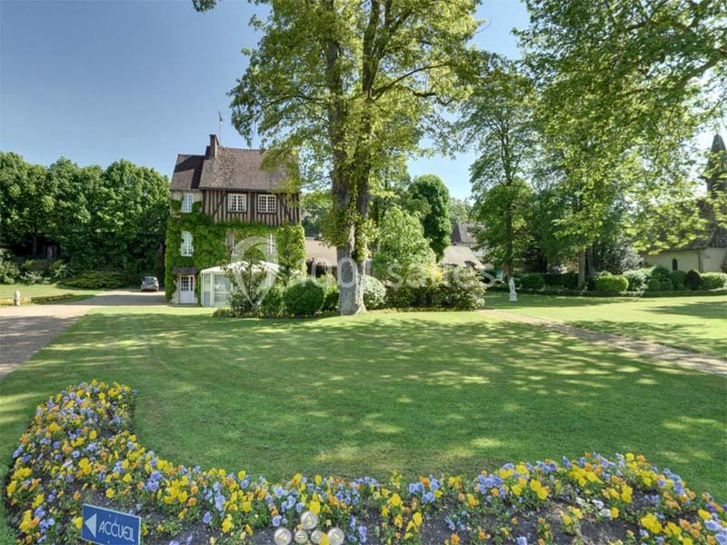 Jardin verdoyant avec parterre fleuri au premier plan et bâtiment couvert de lierre en arrière-plan.