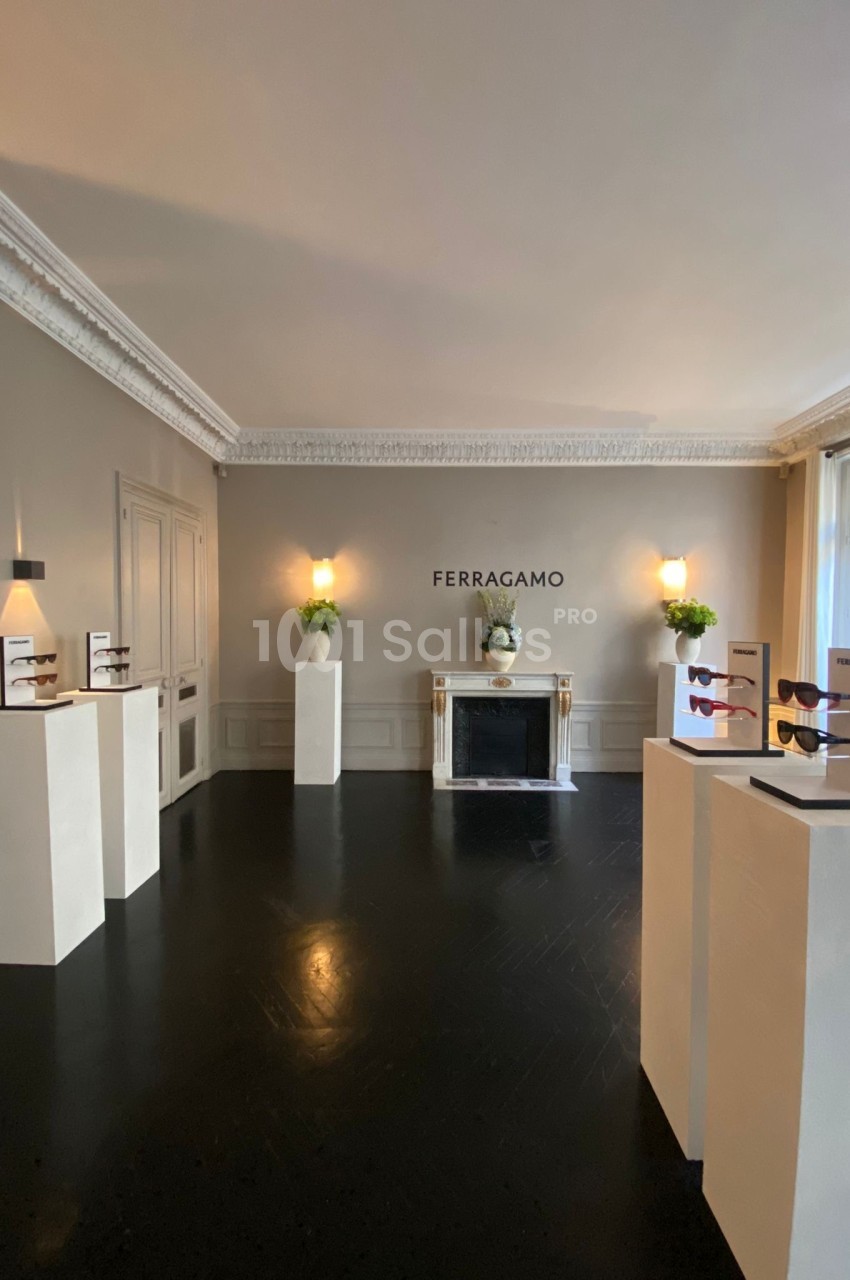 Salle d'exposition lumineuse avec des présentoirs de lunettes et une cheminée décorative, logo Ferragamo au mur.