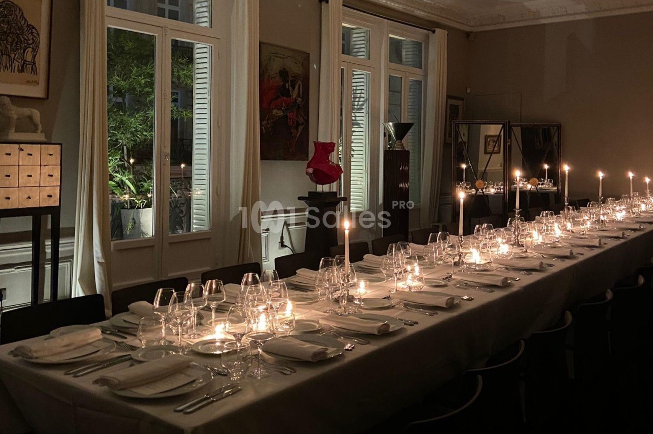 Table élégamment dressée avec des bougies allumées dans une salle à manger aux grandes fenêtres et éclairage tamisé.
