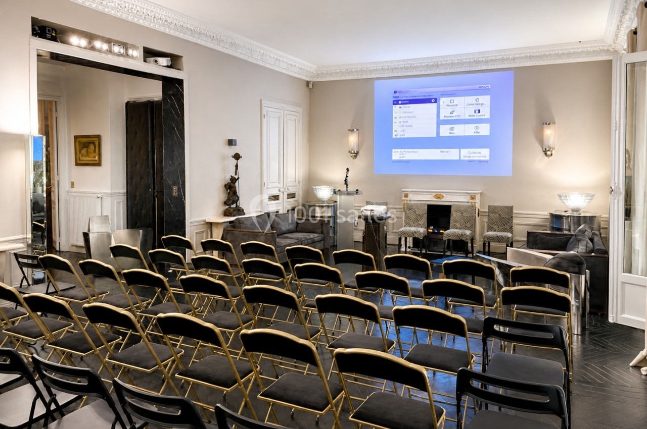 Salle de réunion élégante avec chaises alignées, écran de projection allumé et décoration intérieure raffinée.