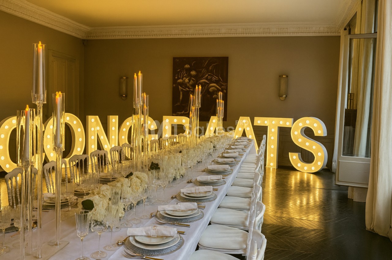 Grande table de réception élégamment dressée avec des chandeliers et des lettres lumineuses formant ’CONGRATS’ en arrière…