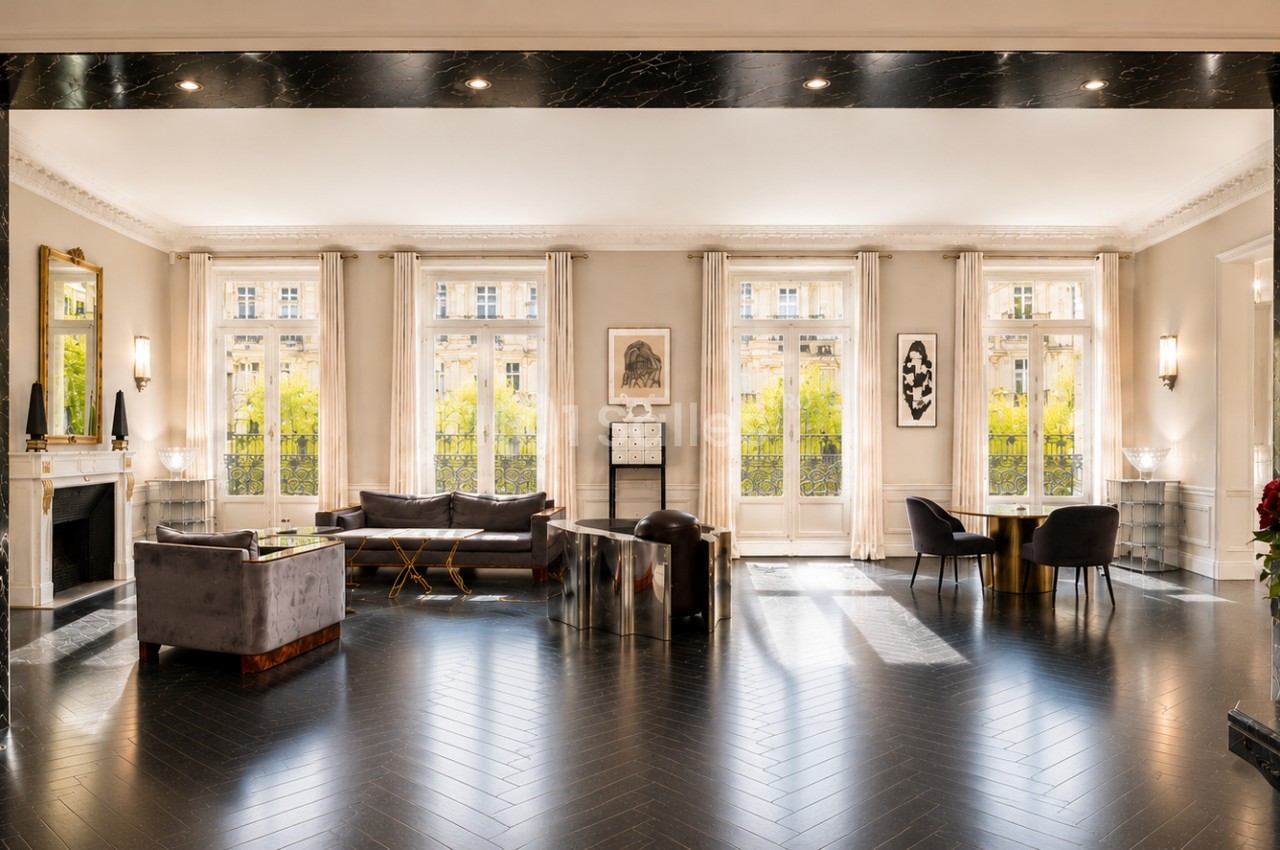 Salon spacieux et lumineux avec parquet sombre, mobilier élégant, grandes fenêtres et décoration raffinée.