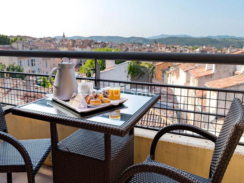Petit-déjeuner avec viennoiseries, jus d'orange et café sur une table en terrasse surplombant des toits de ville.