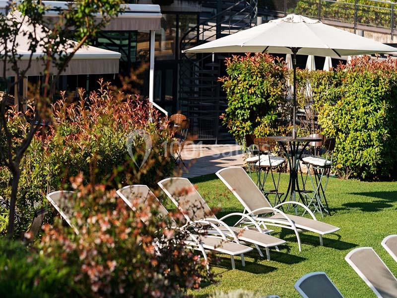 Chaises longues et table avec parasol disposées sur une pelouse entourée de végétation près d'un bâtiment moderne.
