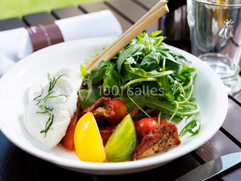 Assiette de salade composée avec roquette, tomates variées, burrata et tomates séchées, servie en extérieur.