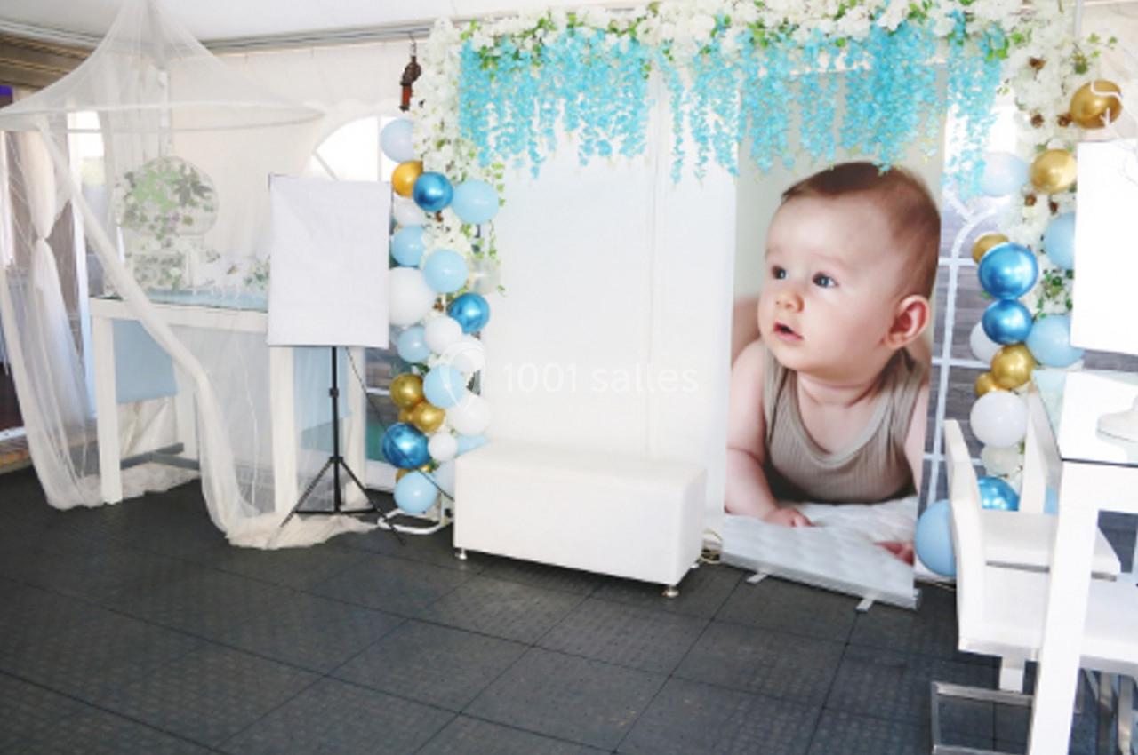 Décoration de fête avec ballons colorés, fleurs suspendues et une grande photo d'un bébé en arrière-plan.