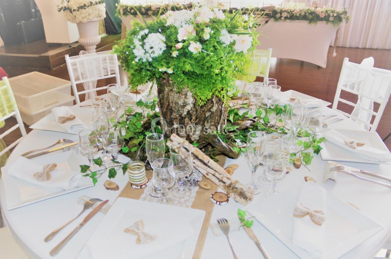 Table décorée dans un style champêtre avec un centre de table en tronc d'arbre, fleurs blanches et verdure.