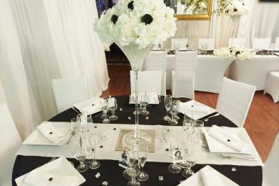 Salle de réception décorée en noir et blanc avec tables dressées, chaises blanches et lanternes suspendues.