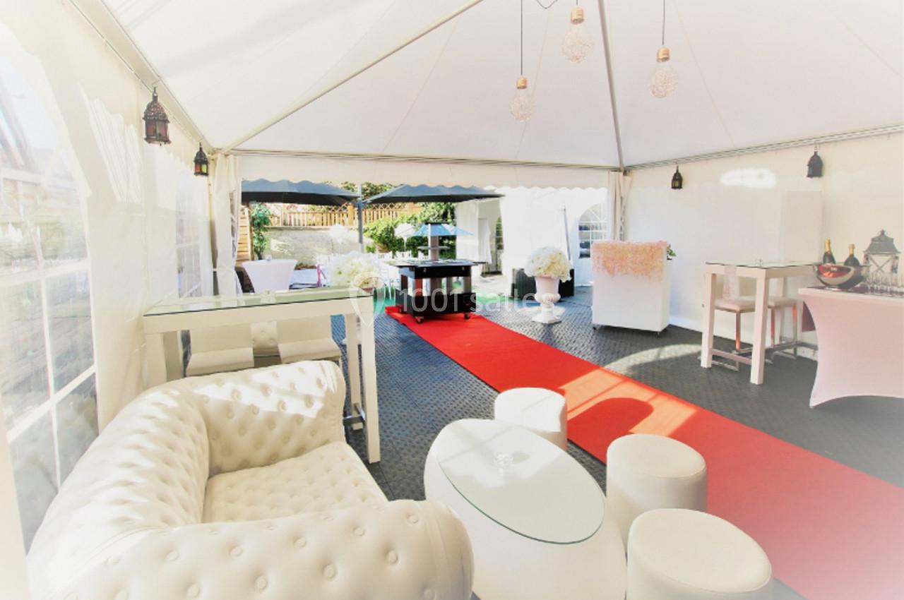 Intérieur d'une tente événementielle avec mobilier blanc, tapis rouge et décoration lumineuse.