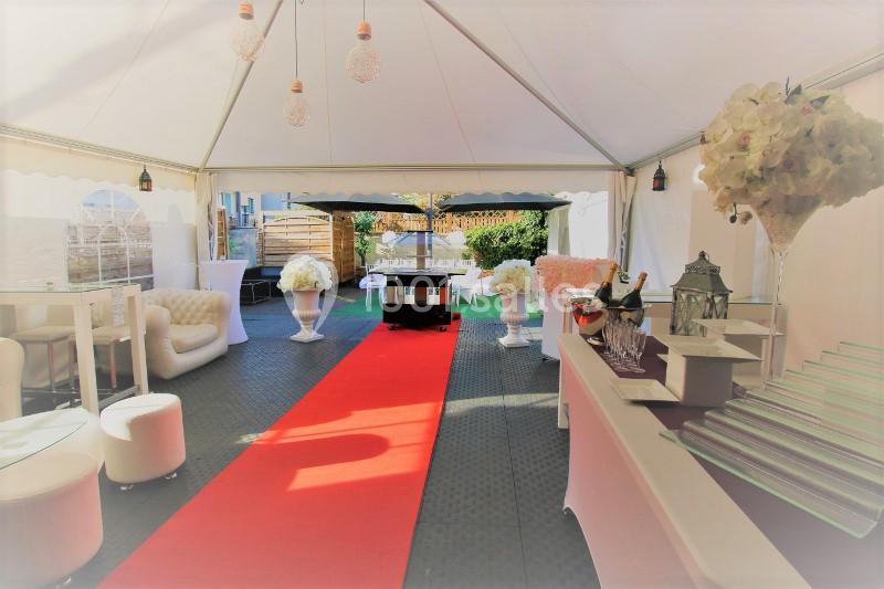 Intérieur d'une tente de réception avec tapis rouge, mobilier élégant, décorations florales et table de buffet.