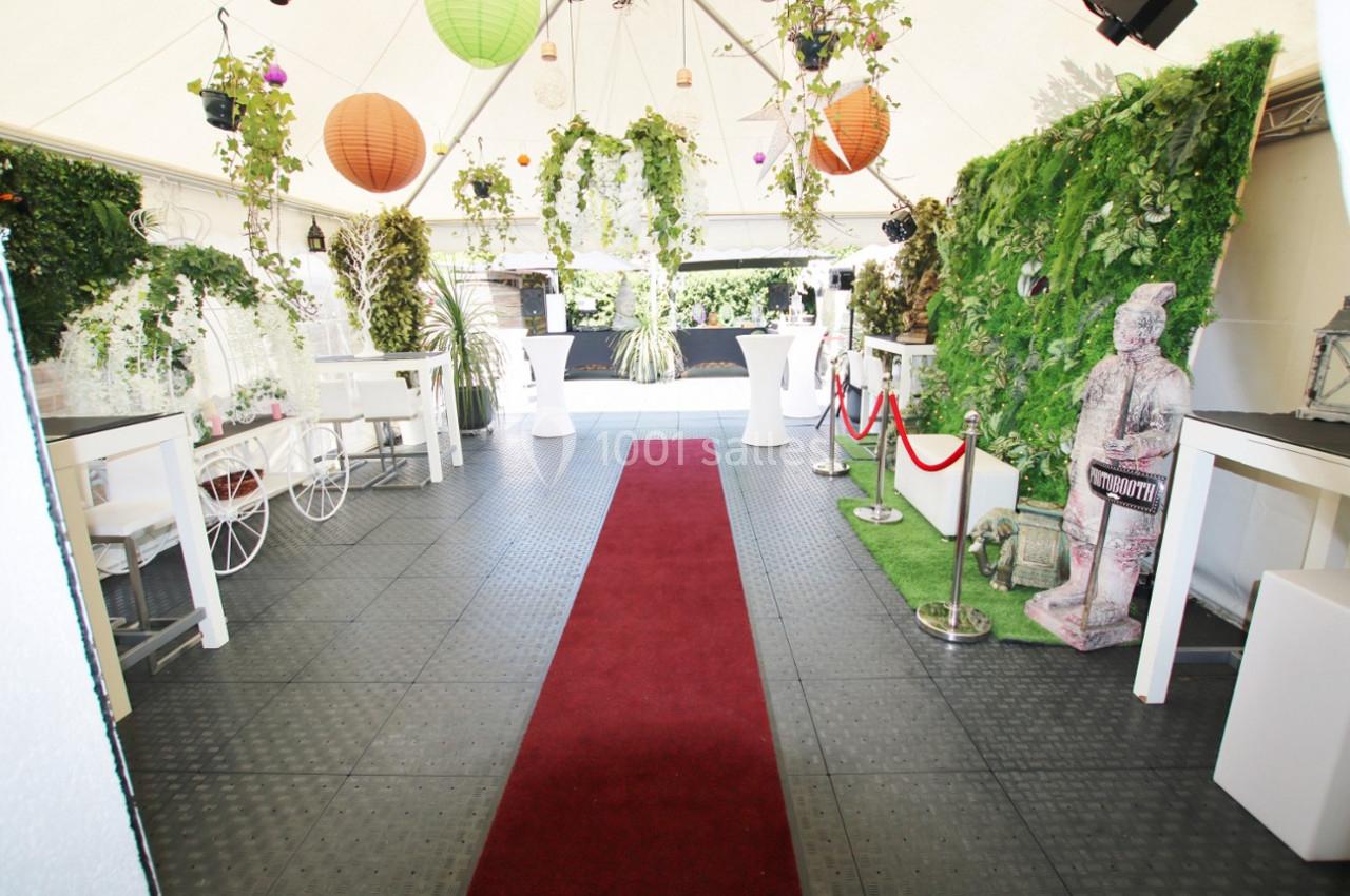 Décoration intérieure d'une tente avec tapis rouge, plantes suspendues, lanternes colorées et statues décoratives.