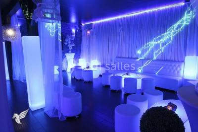 Salle de réception décorée en noir et blanc avec tables dressées, chaises blanches et lanternes suspendues.