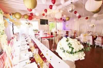 Salle de réception décorée en noir et blanc avec tables dressées, chaises blanches et lanternes suspendues.