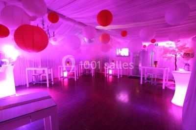 Salle de réception décorée en noir et blanc avec tables dressées, chaises blanches et lanternes suspendues.