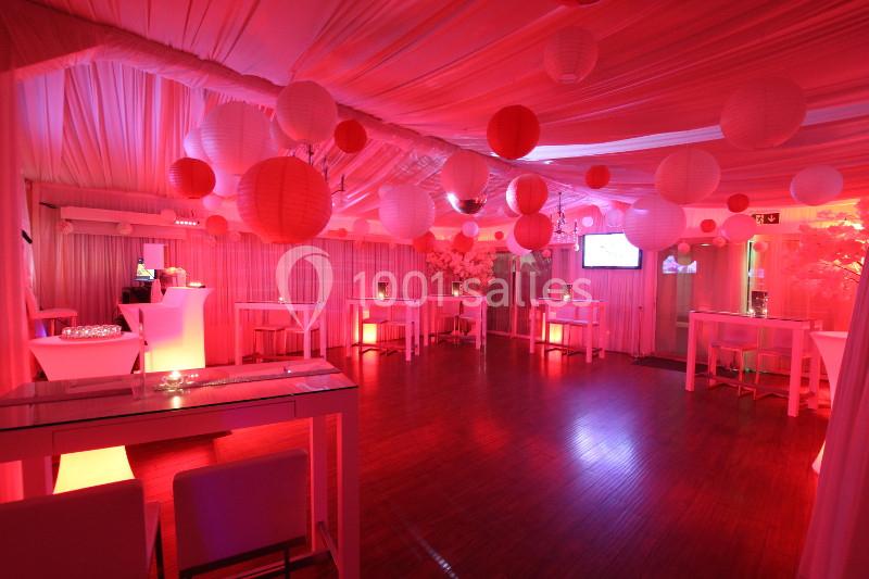 Salle décorée avec des lanternes rouges et blanches, éclairage tamisé, tables hautes et ambiance festive.