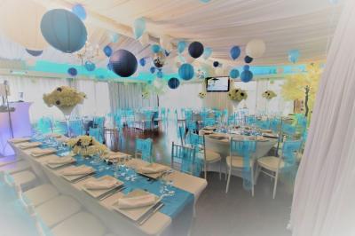 Salle de réception décorée en noir et blanc avec tables dressées, chaises blanches et lanternes suspendues.