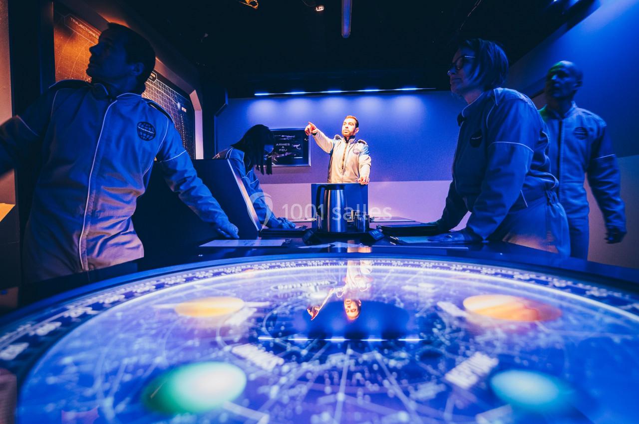 Des personnes en combinaison analysent des données sur une table interactive lumineuse dans une salle au décor futuriste.