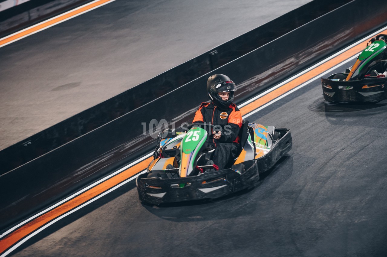 Une personne en karting portant un casque et une combinaison orange sur une piste intérieure.