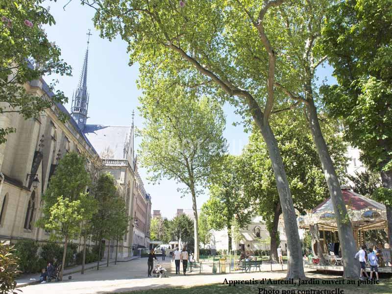 Jardin public avec arbres, allées, manège et église en arrière-plan par une journée ensoleillée.
