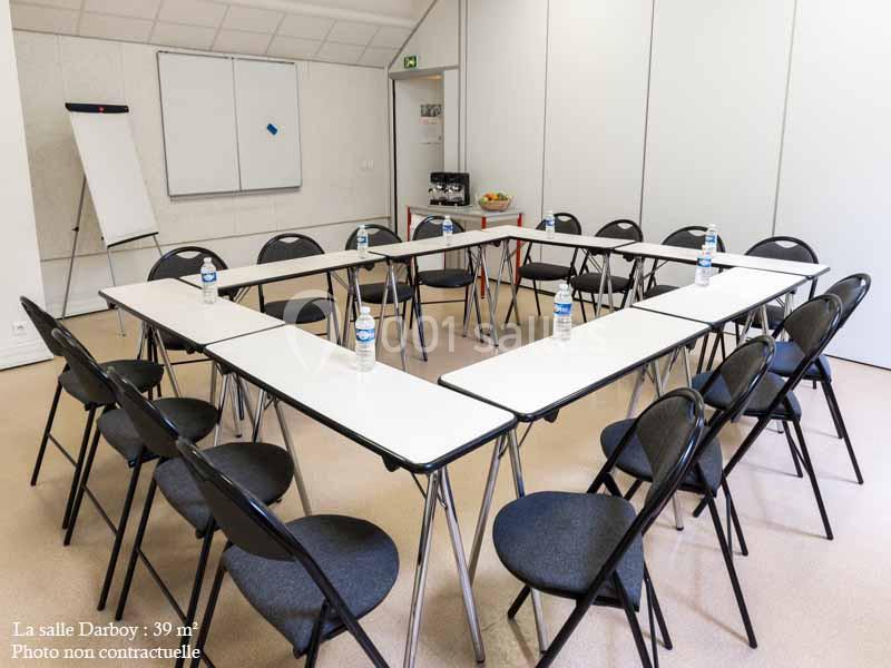 Disposition en U de tables blanches avec chaises noires dans une salle de réunion équipée d'un tableau et d'une fontaine à…
